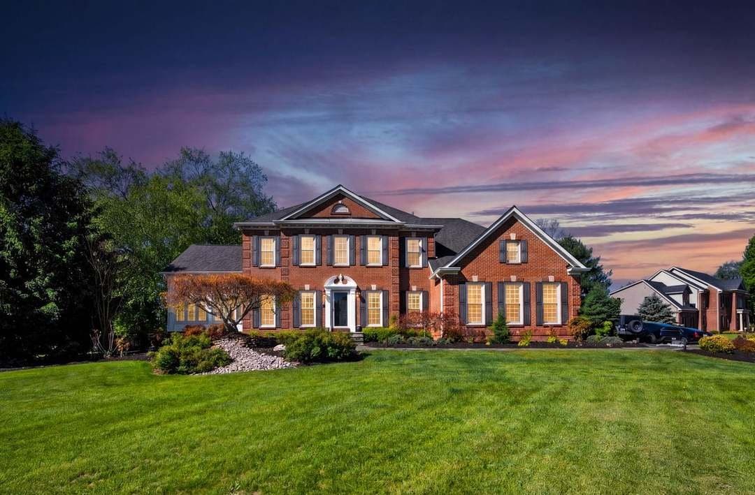 Twilight exterior photograph of a colonial home at dusk with warm interior lighting